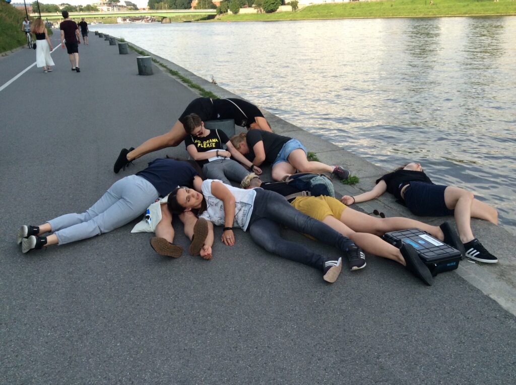 Group of people lying on the riverside boulevard, posing next to a black suitcase