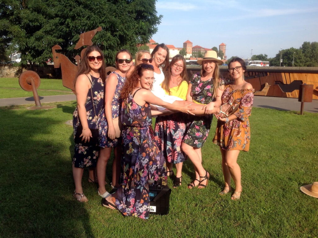 Group of women in summer dresses on the grass holding one of them up, Wawel in the background