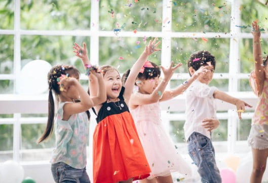 Children jump with raised hands amid falling confetti