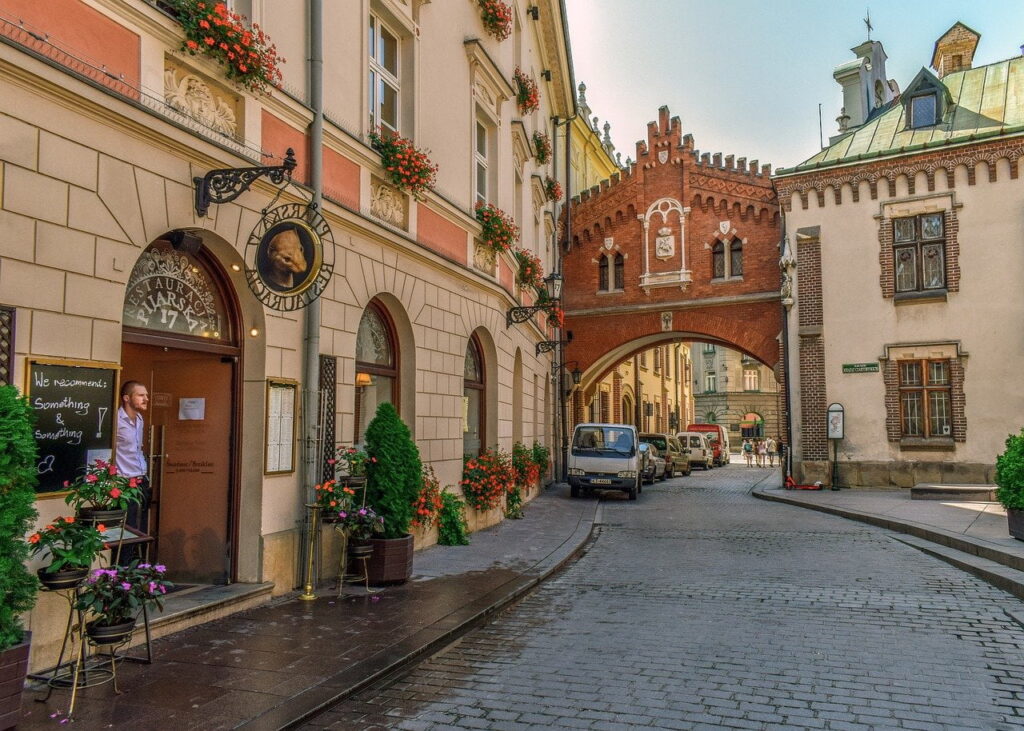 Brukowana uliczka z restauracją „Pijarska 17” i ceglanym łącznikiem nad ulicą