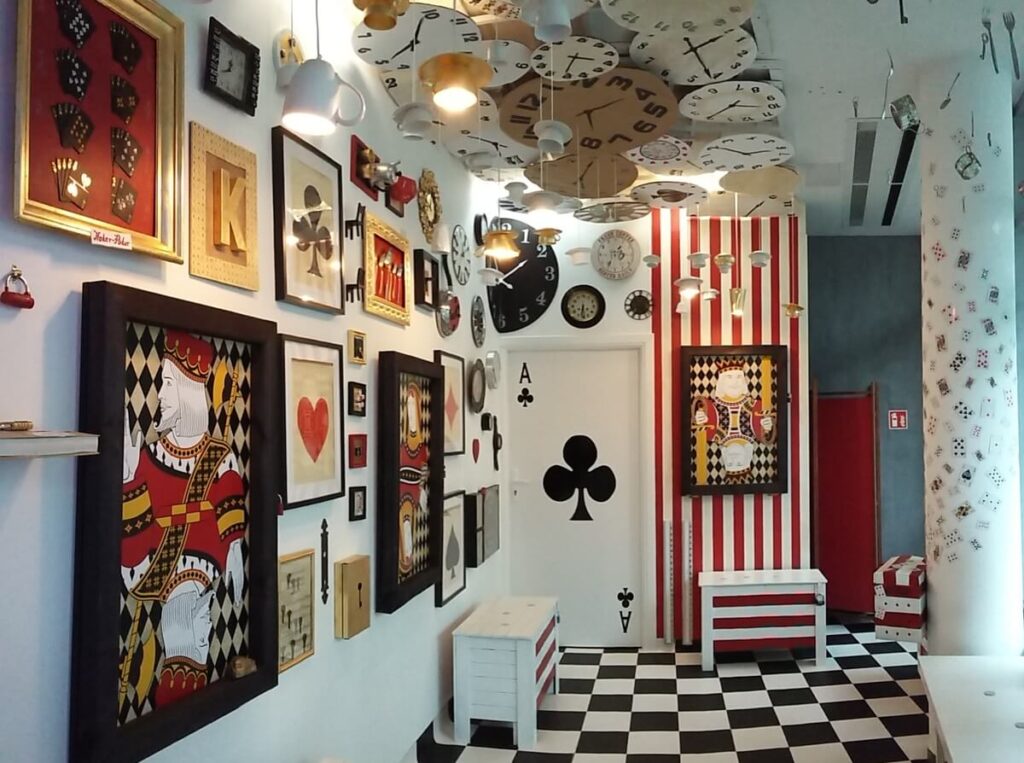 Room with paintings of playing card figures, clocks on the ceiling and a chequered floor
