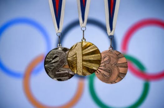 Złoty, srebrny i brązowy medal z cyframi 1, 2 i 3 na tle kół olimpijskich