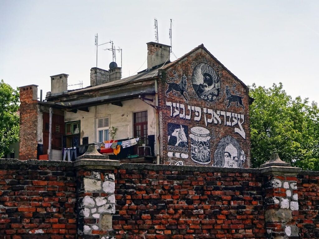 Mural z napisami i postaciami na ceglanej ścianie budynku za murem.