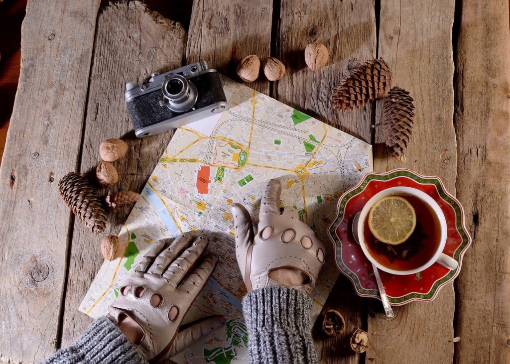 Hands in leather gloves on a city map next to a camera, pine cones and lemon tea