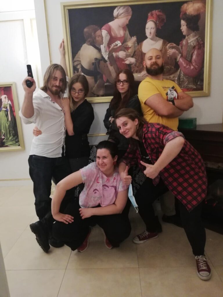 Six players pose in front of a gold framed painting, one holding a toy gun