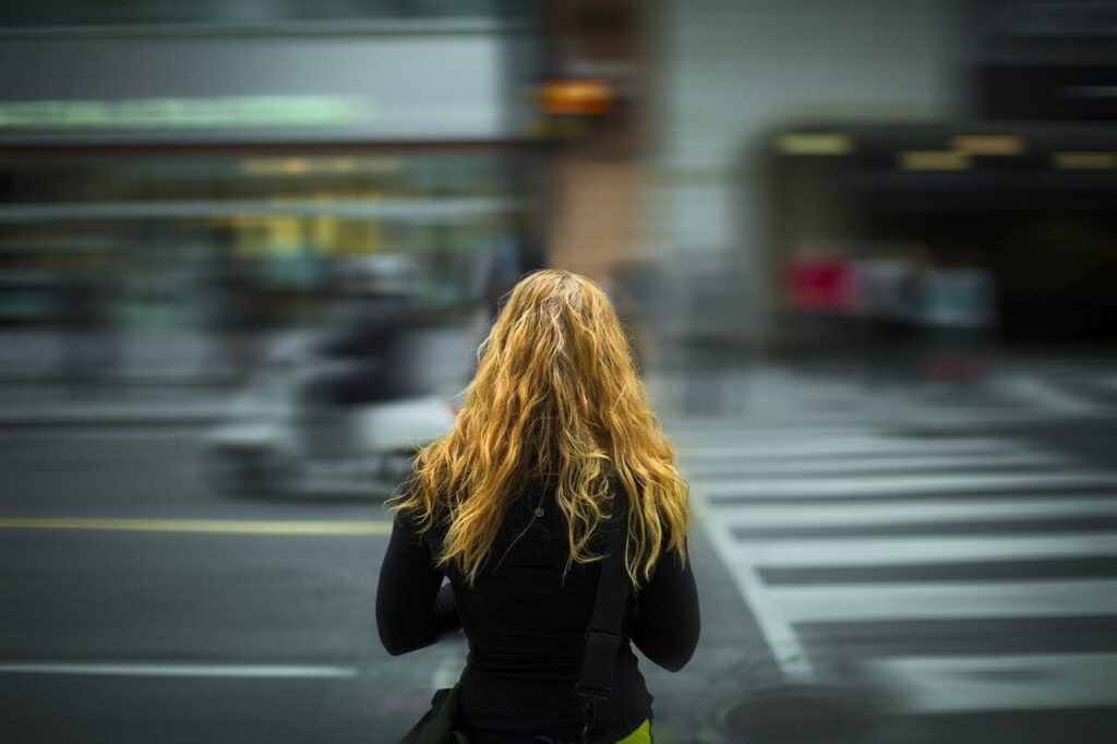 Woman with long red hair stands with her back to the camera at a pedestrian crossing
