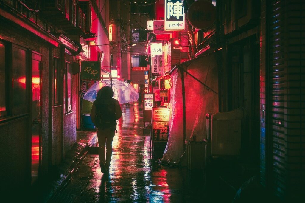 Person with a transparent umbrella walks down a wet street full of neon signs with Asian lettering