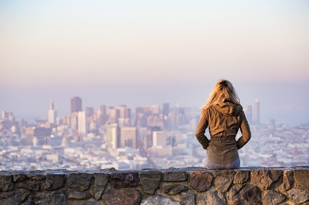Woman sitting on a stone wall looks out over a city skyline with high rises