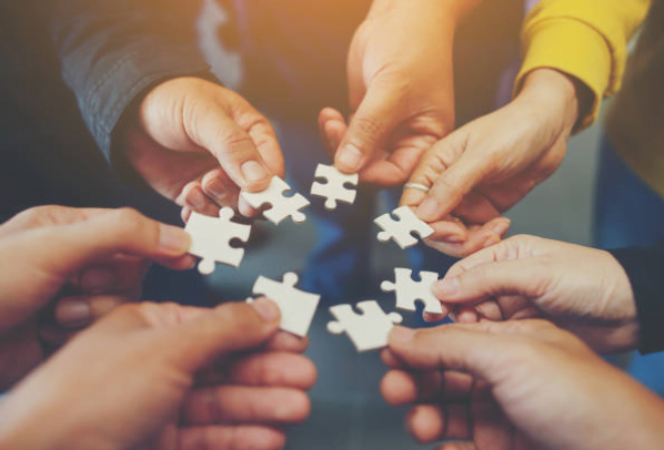 Kilka dłoni trzyma białe elementy puzzli ułożone w krąg